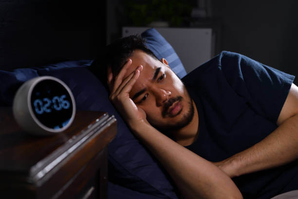 Depressed young Asian man lying in bed cannot sleep from insomnia