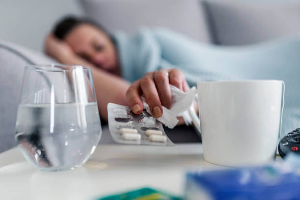 Unhealthy sick Caucasian woman suffers from insomnia or headache during the day, takes sleeping pill while laying in bed with glass of water, depressed girl holds antidepressant medications, painkiller for menstrual pain, close up. Photo of Stressed woman drinking pill or medicine with glass of water on bed at home after wake up in the morning
