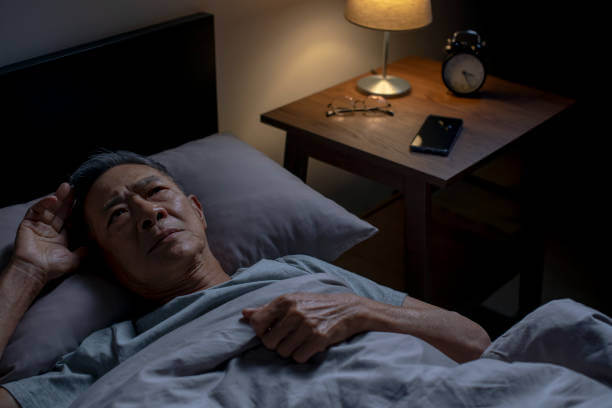 Depressed senior Asian man lying in bed cannot sleep from insomnia