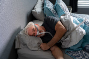 A 60-year-old man sleeps with a CPAP machine in bed to treat his sleep apnea