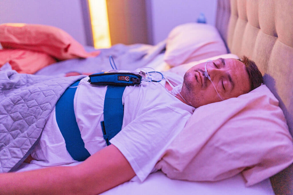 A man is using a sleep study device to monitor sleep apnea.